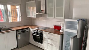 Uma cozinha moderna com armários brancos, lava-louças, forno, fogão e geladeira.