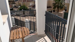 Uma varanda com mesa de madeira, guarda-corpo de metal e vista para o mar e edifícios.