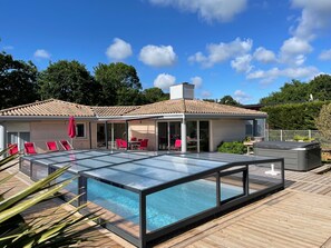 Una casa moderna con piscina cubierta de vidrio, muebles de exterior rojos y una terraza de madera.