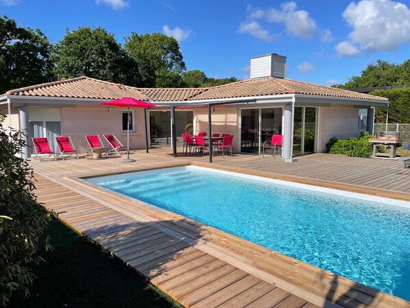 Zona junto a la piscina con piscina, terraza de madera y sillas de descanso rojas.