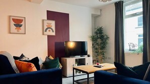 Un salon moderne avec un téléviseur à écran plat, une table basse en bois et deux canapés bleus.