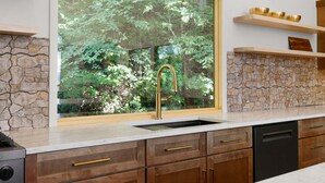 A kitchen with a stone backsplash, a window with a view of greenery, and wooden cabinets.