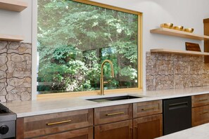 A kitchen with a stone backsplash, a window with a view of greenery, and wooden cabinets.