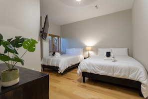 Habitación de hotel con dos camas, una planta en maceta y un televisor montado en la pared.
