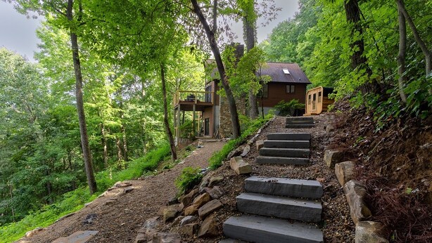 Una escalera de piedra que conduce a una cabaña de madera rodeada de vegetación exuberante.