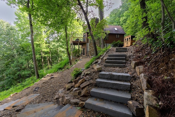 Una escalera de piedra que conduce a una cabaña de madera rodeada de vegetación exuberante.
