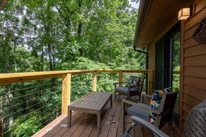 A wooden deck with a table and two chairs, surrounded by lush greenery.