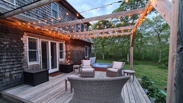 Une terrasse en bois avec des sièges d’extérieur, des guirlandes lumineuses et un jacuzzi.