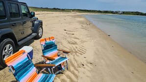 Une plage avec deux chaises de plage à rayures et un VUS garé.
