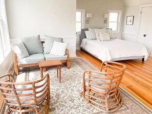 Quarto com uma cama, um sofá, duas cadeiras de vime e uma mesinha.