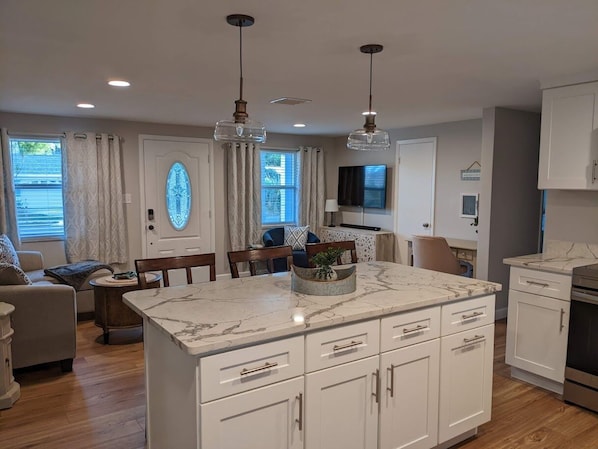 A modern kitchen with white cabinetry, a marble countertop, and pendant lighting.