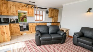 A modern kitchen with wooden cabinets, a black leather sofa, and a striped rug. - Lathkill Barn (Bakewell)