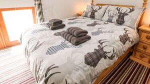 A bed with a patterned bedspread, a wooden headboard, and a nightstand with drawers. - Lathkill Barn (Bakewell)