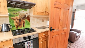 A kitchen with wooden cabinets, a gas stove, a kettle, and a wall-mounted oven. - Haddon Cottage (Bakewell)