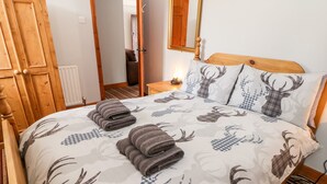 A bed with a checkered deer pattern, a wooden headboard, and a nightstand with a lamp. - Haddon Cottage (Bakewell)