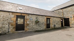 A stone building with a tiled roof, a sign reading "MONSAL COTTAGE," and a small garden area with flowers. - Monsal Cottage (Bakewell)