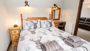 A bed with a deer print duvet, a bedside lamp, a wooden nightstand, a mirror, a chair, and a brown leather sofa. - Monsal Cottage (Bakewell)