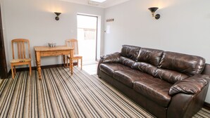 A room with a brown leather sofa, a wooden dining table with two chairs, and a striped carpet. - Monsal Cottage (Bakewell)