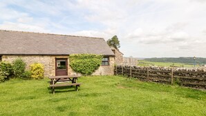A stone cottage with a wooden door, a picnic table, and a stone wall. - Ashford Cottage (Bakewell)