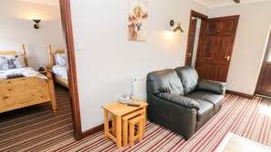 A room with a striped carpet, a wooden bed, a black leather sofa, and a painting on the wall. - Ashford Cottage (Bakewell)