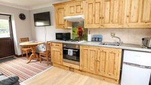 A kitchen with wooden cabinets, a microwave, a stove, and a refrigerator. - Ashford Cottage (Bakewell)