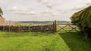 A rural landscape with a stone wall, a wooden gate, and a stone building. - Ashford Cottage (Bakewell)