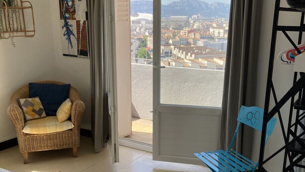 Ein Zimmer mit Blick auf eine Stadtansicht, ein Korbstuhl, ein blauer Sessel, ein Bett und eine kleine Trommel.