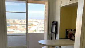 Eine kleine Küche mit Schachbrettmuster, einem Esstisch, zwei Hocker, einer Mülltonne und Blick auf die Stadt durch eine Schiebetür.
