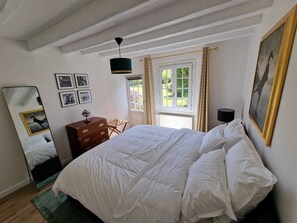 A bedroom with a large bed, a dresser, a mirror, and a window with curtains.