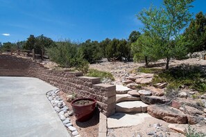 A concrete pathway leading to a brick structure with a wooden fence, surrounded by rocks and sparse vegetation.