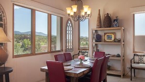 Un comedor con una mesa de madera, sillas rojas, una araña y vistas al exterior.