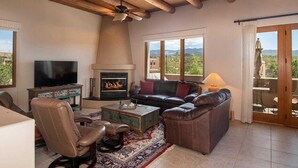 Una sala de estar con chimenea, muebles de cuero, televisor y un balcón con vistas.