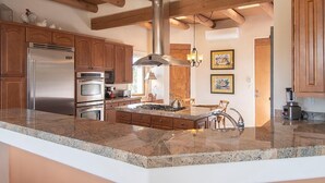 Una cocina con encimeras de granito, electrodomésticos de acero inoxidable, armarios de madera, una isla central e iluminación colgante.