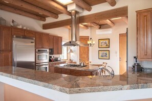 A kitchen with granite countertops, stainless steel appliances, wooden cabinets, a central island, and a hanging light fixture.