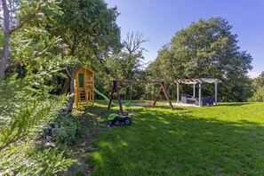 Relax in a serene outdoor space with a swing set, playhouse, and shaded seating area surrounded by lush greenery.