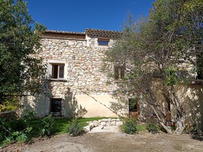 A stone building with a tiled roof, a small window, and a door. - Village house in a green setting (Vinsobres)