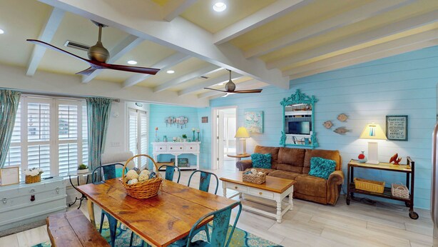 A spacious living room with a wooden dining table, a brown sofa, and a blue accent wall. - Lighthouse Unit B - 2 bedrooms, 2 bathrooms (Jekyll Island)