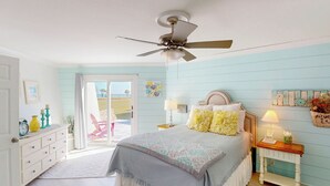 A bedroom with a bed, a ceiling fan, a nightstand, a dresser, and a view of the outdoors through a sliding glass door. - Lighthouse Unit B - 2 bedrooms, 2 bathrooms (Jekyll Island)