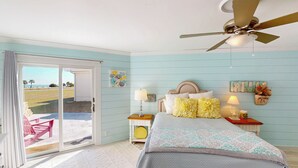 A bedroom with a bed, a ceiling fan, a nightstand, a lamp, and a view of the outdoors through a sliding glass door. - Lighthouse Unit B - 2 bedrooms, 2 bathrooms (Jekyll Island)