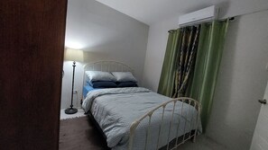 Een slaapkamer met een bed, een staande lamp en een raam met gordijnen.