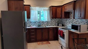 A compact kitchen with wooden cabinets, a refrigerator, a microwave, and a stove.