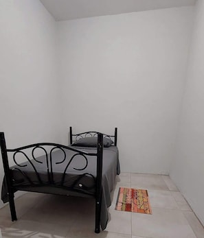A small, single-bed room with a metal bed frame and a plain wall. - Santa Fe (Port of Spain)