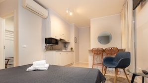 A modern bedroom with a large bed, a small kitchenette, and a dining area with two chairs.