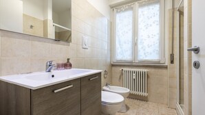 A bathroom with a white sink, two toilets, a mirror, and a window with a floral curtain.