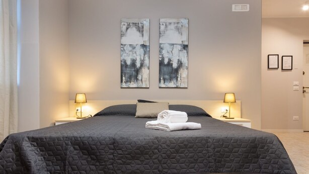 A neatly made bed with a dark quilt, two bedside lamps, and two abstract paintings on the wall.