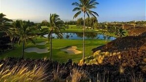 Un campo de golf con un estanque, palmeras y un cielo despejado.