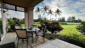 An outdoor patio with a table and chairs, a view of palm trees, and a well-maintained garden. - Colony Villas At Waikoloa Beach Resort #1305 3 Bedroom Villa by RedAwning (Waikoloa)