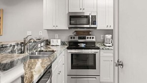 A modern kitchen with white cabinets, a stainless steel oven, a microwave, a coffee maker, and a granite countertop. - Romar Beach 112 2 Bedroom Condo by RedAwning (Orange Beach)