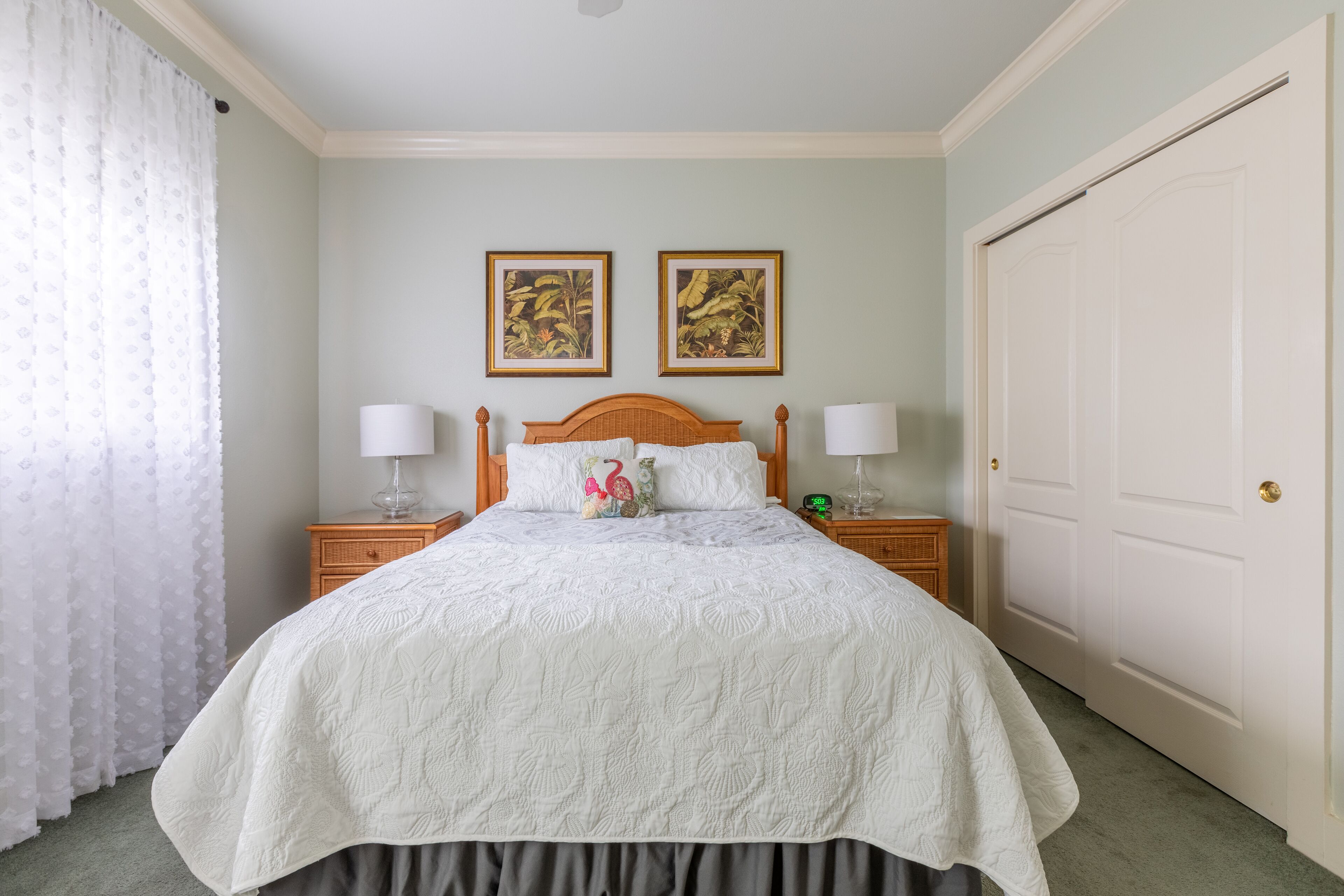 A neatly made bed with a white bedspread, two wall-mounted paintings, and a closed door.