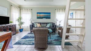 A living room with a sofa, a TV, a coffee table, and a bookshelf. - Coastal Tranquility: Beautiful Condo Offering Poolside Serenity Near Beach (Pensacola)